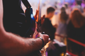 Concert view of an electric guitar player with vocalist and rock band performing in a club, male musician guitarist on stage with audience in a crowded concert hall arena