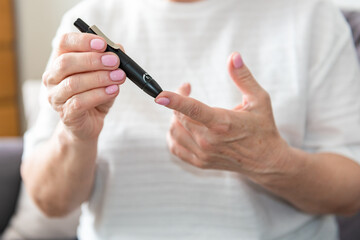Old woman hands using lancet on finger to check blood sugar level, diabetes concept, health care
