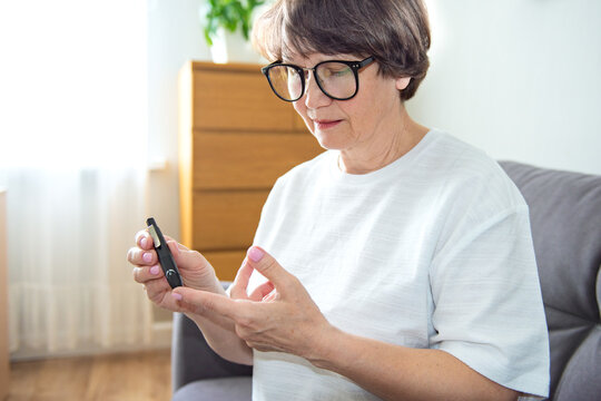 Diabetic mature woman checking blood glucose levels with glucose meter at home. Diabetes and elderly health are concept