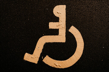 Top view of yellow wheelchair sign painted on the asphalt road marking a car park for disabled or...