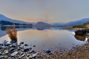 SMOKE FROM A WINTER GRASSFIRE reflects in a drakensberg mountain lake - 633340614
