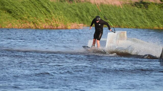 Young man wakeboarding in the park making difficult pro level wakeboard tricks. Extreme water sports. Action time in summer. Wakeboarder making tricks. 