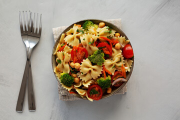 Yummy Homemade Vegan Pasta Salad with Tomato, Onion, Carrot, Broccoli, Chickpeas and Parsley in a Bowl, top view.