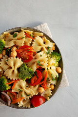 Yummy Homemade Vegan Pasta Salad with Tomato, Onion, Carrot, Broccoli, Chickpeas and Parsley in a Bowl, top view.