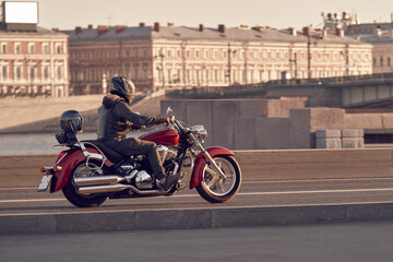 A motorcyclist in a leather jacket rides a red motorcycle on city roads. Biker in a helmet on a...