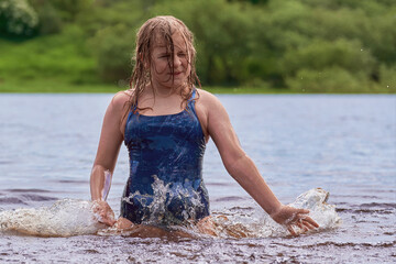 A child of 10-12 years old pulled out of the water, outdoors. A school-age girl swims and has fun playing in the river on a hot summer day, close-up.
