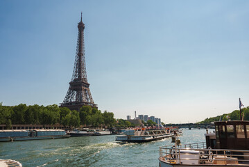 Sunny view of the Eiffel Tower with white boats on the Seine River in Paris at noon.