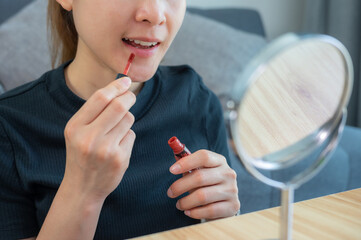 Cropped shot of woman while applying cream lipstick on her lips.