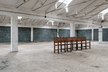 White hall of an industrial building with walls crammed with formulas on a green chalkboard, and a row of wooden chairs stands in the space