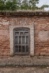 Wooden door in a dilapidated brick wall with grass on top