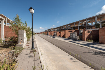 Street of unfinished houses with a crooked lamppost against a blue sky