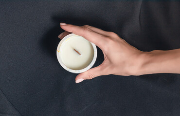 Woman hand holds a decorative scented candle on a black background