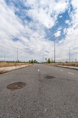 Abandoned street with two sewer cover against blue overcast sky, bottem up view of asphalt