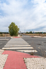 Obraz premium Abandoned street with a tree and a crosswalk with red tiles , against a blue overcast sky