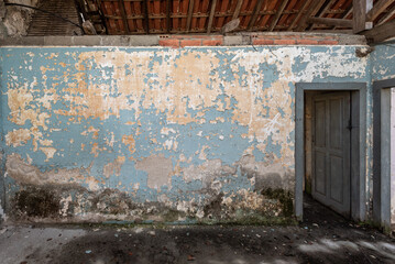 Wall in an abandoned house with flaking blue paint and an open gray door