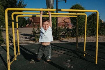 preschool child boy plays on horizontal bars on the playground in the park in summer