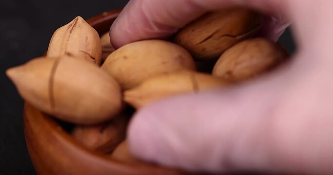 take a cracked unpeeled pecan close-up on the table, a pile of pecans in the shell
