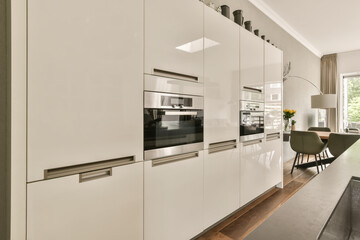 a modern kitchen with white cabinetry and wood flooring in an open plan living room is visible on...