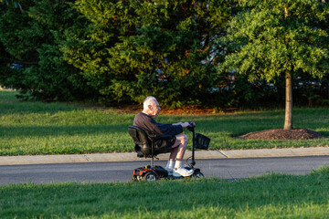 Solomons, Maryland, USA A senior retired man rides an electric battery-driven mobility scooter in a park.