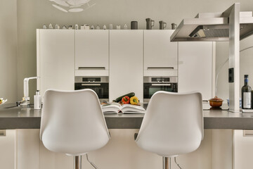 two white chairs in a kitchen with a book on the counter top and an open door leading to another room