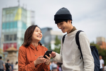 街中でスマートフォンを見ている笑顔のカップル