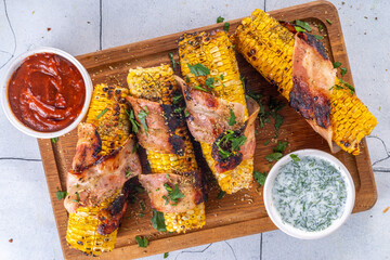 

Bacon wrapped grilled corn on the cob, southern american, mexican bbq food recipe, with sauces on white tile background