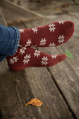 Outdoor product photo of men's burgundy snowflake patterned dress socks. The man is wearing jeans with them and is sitting on a wooden deck.