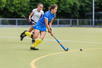 Young female player running with ball in attack on the pitch in field hockey game