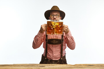 Portrait of young emotional man in hat, wearing traditional Bavarian clothes, holding beer mug...