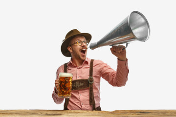 Portrait of man wearing traditional Bavarian or German oyfit shouting in vintage megaphone and...