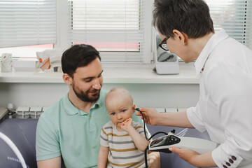 Child having hearing exam at otolaryngologist. Examining little patient, hearing test of infant kid by audiologist. Father with baby visiting doctor for checkup