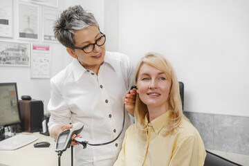 Woman patient having checkup of hearing at doctor audiologist. Middle age woman visiting...