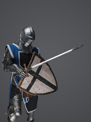 Blue surcoat-wearing medieval knight actively swinging sword in battle on gray background