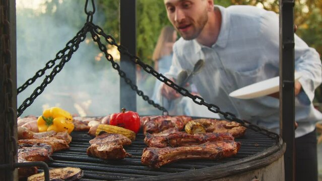 
A group of happy people are resting in a country house. Enjoy cooked fresh meat on the grill. Cheerful rest, with cooking meat and drinking drinks.