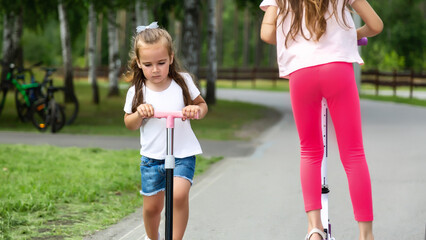 little girls riding scooters in summer park, children sports