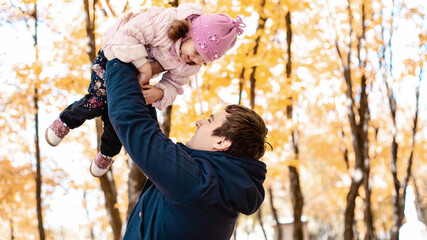 Cute little girl playing with dad outdoors. A happy child is tossed up in an autumn Park. The kid...