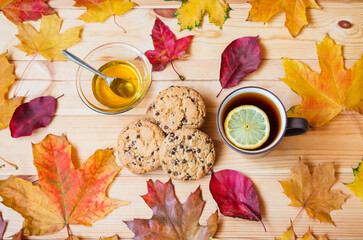 Cup of tea, honey, cookies and autumn leaves on wooden table. Top view.