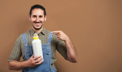 Happy smiling young male farmer points to fertilizer bottle mockup over brown background with copy...