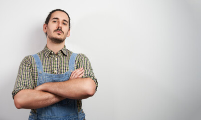 confident young male farmer with overalls and arms crossed over grey background with copy space
