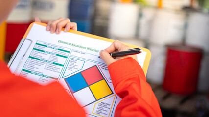 A safety officer is checking on the hazardous material checklist form with chemical storage area at...