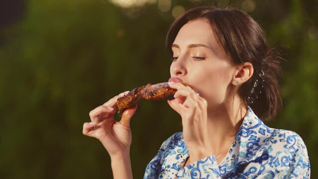 people, diet, cooking and nutrition concept - hungry young woman eating meat in nature