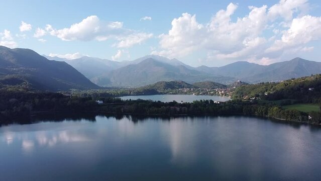 Bird eye view of two lakes called Laghi di Avigliana. Aerial drone view of lakes with calm water surrounded by mountain ranges in Italian Alps in summer. Water surface reflects clouds, Piedmont, Italy