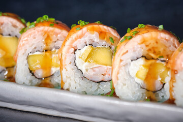 Appetizing sushi rolls with fresh salmon and sauce on marble plate