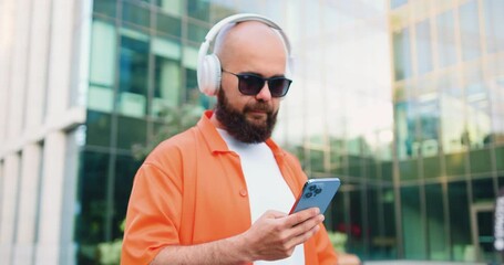 Hipster man in white casual headphone walking beside his bicycle and using smartphone in sunny weather. Chatting while cycling. Modern lifestyle, connection. - Powered by Adobe