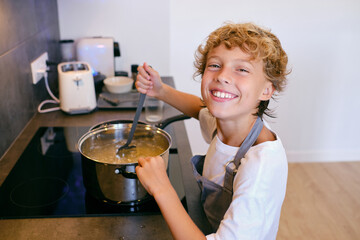 Content boy stirring pasta in pot while cooking in kitchen