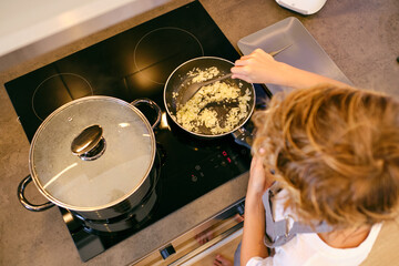 Unrecognizable person stirring onion in pan on stove top - obrazy, fototapety, plakaty