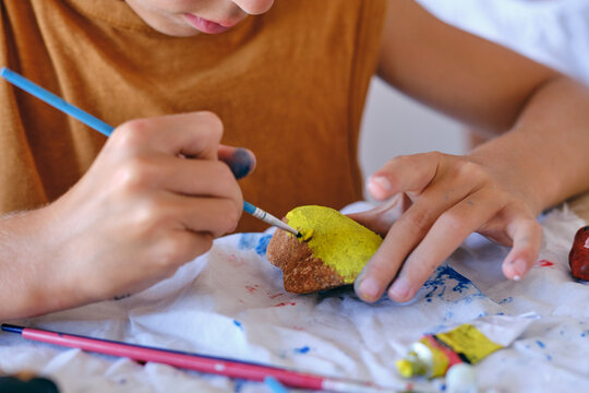 Crop child painting rock with yellow color