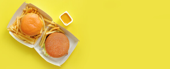 Open cardboard box with burgers and french fries on a yellow background, top view. Fast food restaurant. Copy space