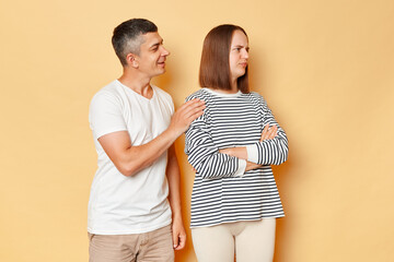 Smiling man trying to reconcile with offended woman wearing casual clothing standing isolated over...