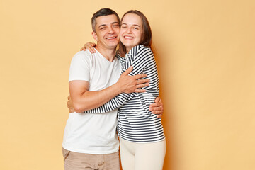 Fototapeta premium Cheerful joyful man and woman wearing casual clothing standing isolated over beige background hugging each other expressing love gentle and romantic feelings.